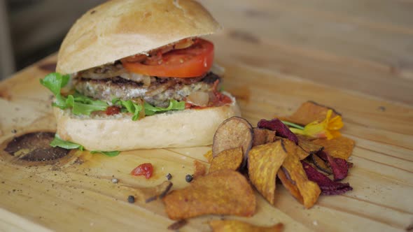 Slow pan of farm-stall beef burger and dry vegetable chips alt