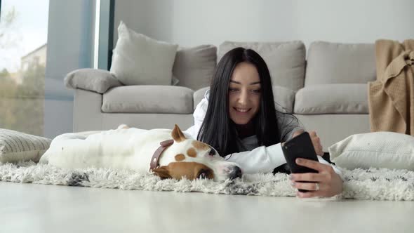 Young Woman Takes a Selfie with Her Dog and Use Phone in a Beautiful Modern Apartment alt