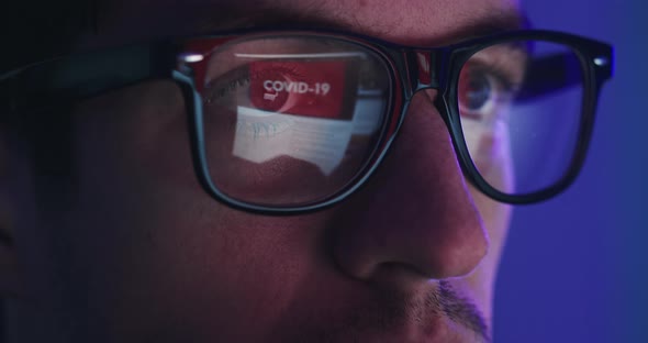 Closeup Portrait of Man in Eyeglasses Late at Night Scrolling News Abous Coronavirus in Front of alt