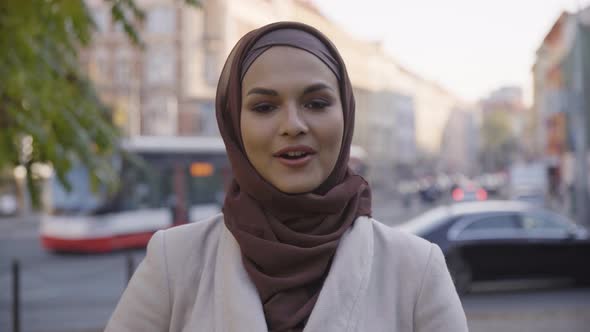 A Young Beautiful Muslim Woman Talks to the Camera with a Smile in a Street in an Urban Area alt