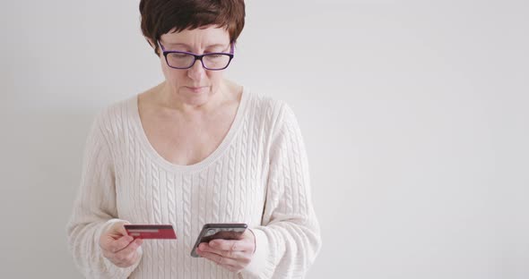 Brunette Woman in Glasses Makes Purchases in the Online Store with Phone and Credit Card alt