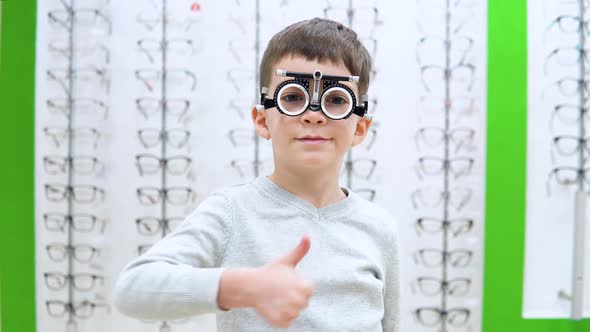 Little Boy Stands on a Background of a Showwindow with Frames for Spectacles with the Device  alt