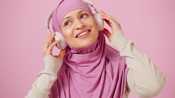 Portrait of Muslim Lady in Hijab Enjoying Music in Headphones Dancing Over Pink Studio Background alt