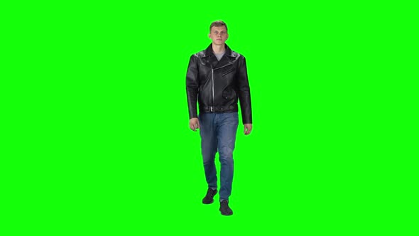 Young Man in Black Leather Jacket, Jeans and Sneakers Going Against a Green Background. Slow Motion. alt