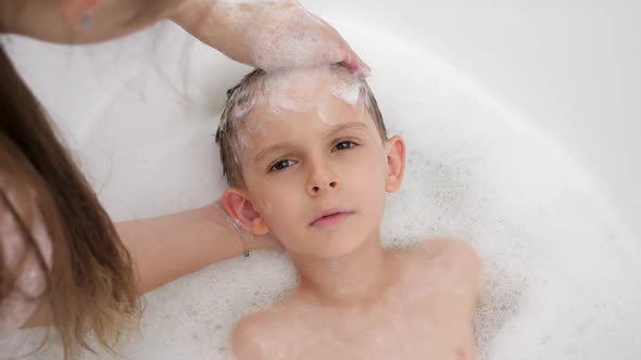 Portrait of Smiling Little Boy Looking at Mother While She Washes His Hair with Shampoo in Bathroom alt