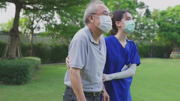 Asian young woman nurse support disabled senior elderly man on wheelchair to walk with cane at park. alt