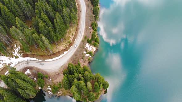 Aerial view of car driving through the forest and the lake on the side. Beautiful mountain road. alt