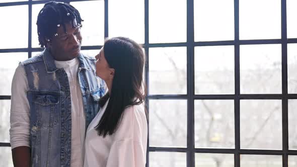 Mixedrace Couple Standing Next to the Window Embracing and Looking at Each Other alt