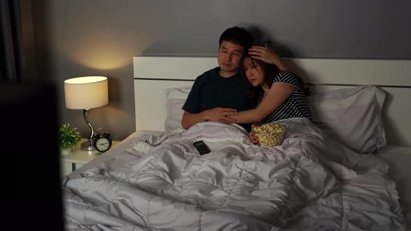 sad young couple watching television and crying on a bed at night (romantic movie)