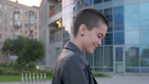 Young Woman with Shaved Hair Walking Against Urban Background alt