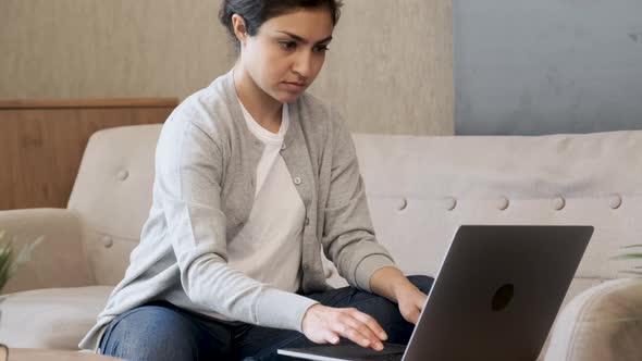 Close up Pretty young lady sitting on couch at home, using laptop, watching videos online, chatting alt
