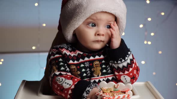 Cute Serious Little Baby Boy in Santa Hat Playing with Toy Gingerbread House alt
