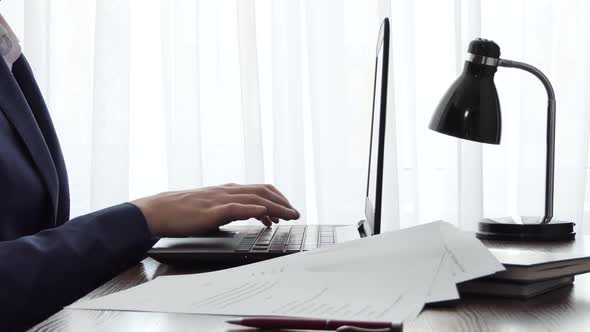 A Man Working with a Laptop on a Desktop Next to a Window alt