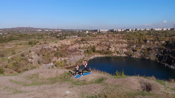 Aerial Orbiting Shot of Slender Young Mother Do Yoga Exercises with Child Daughter on High Hill By