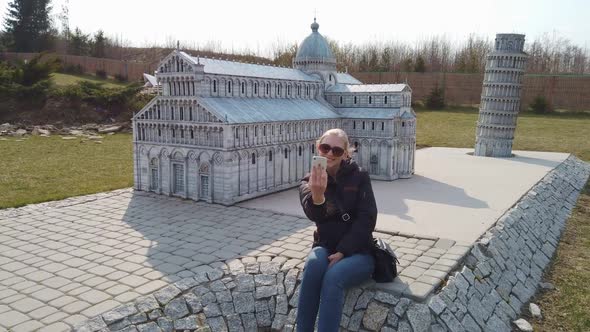 Woman Takes a Selfie Near a Miniature Model of the Old Cathedral, Europe. Park of Miniatures alt