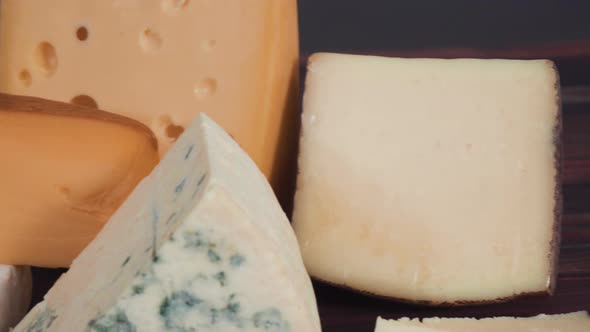 Large wedges of gourmet cheese on a rustic wood background. alt