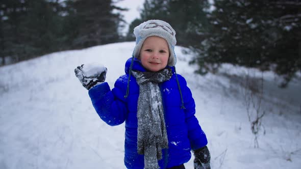 Portrait of a Cute Little Boy with a Snowball in His Hands Plays with Snow in Winter Forest While