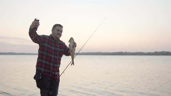 Male Angler Taking Selfie with Fish Near Water