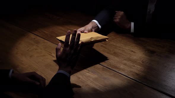 Businessman rejecting money in the envelope secretly offered by his partner in dark room