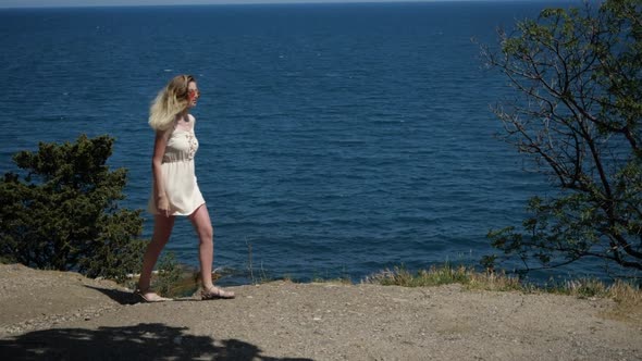 A Woman Makes a Promenade Along the Coast of the Sea Enjoying the Sun's Rays