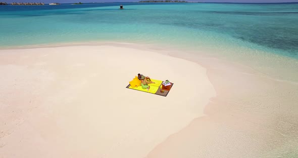 Aerial drone view of a man and woman couple having a picnic meal on a tropical island beach alt