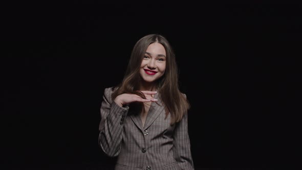 A stylish young brunette in a jacket smiles and poses for the camera on a black background. alt