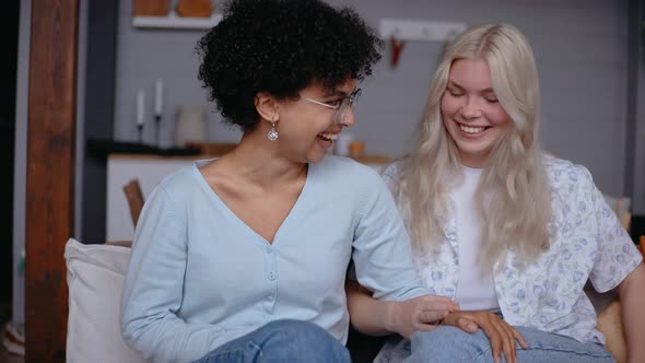 Beautiful Lesbian Couple Laugh Together Sitting on a Couch Holding Hands