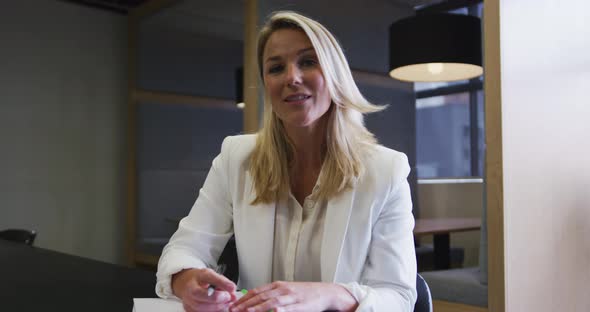 Caucasian businesswoman having video chat going through paperwork in modern office alt