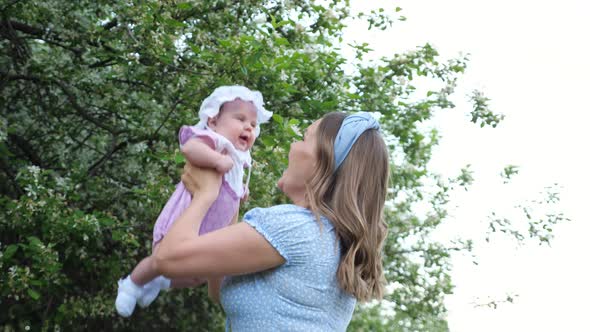 Joyful Blonde Mother Tosses Funny Baby Girl and Kisses Kid alt