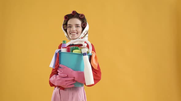 A Happy Young Brunette Woman Holds a Bucket of Cleaning Products and Smiles