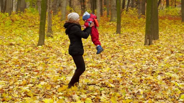 Young woman and boy 2 years have fun in the autumn park. Mom holds his son by the hand