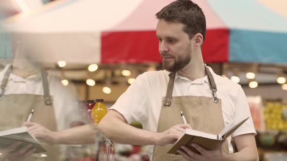 Male Grocery Shop Seller Making Notes in Notepad alt