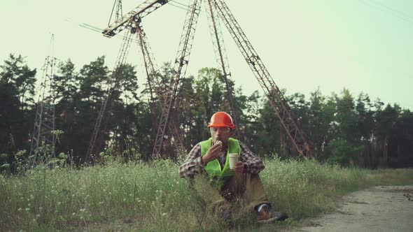 Engineer Having Lunch Near Power Lines and Electricity Pylons in the Field alt