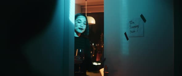 Young woman greeting friends while opening a door in blue lights alt