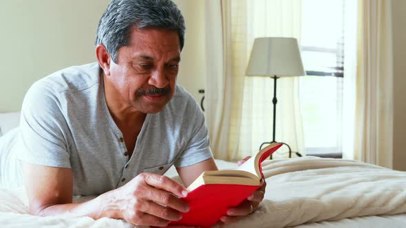 Senior man reading a noel in bedroom 4k alt