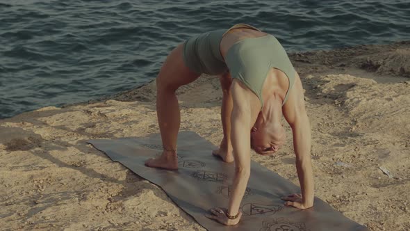 Blond Caucasian Yoga Teacher Practicing and Mastering Wheel Pose on a Cliff in Front of the Sea