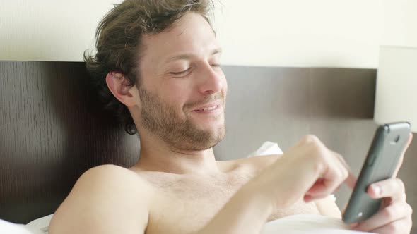 Man lying in bed looking at smart phone