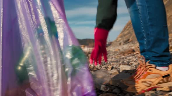 Earth Day. A female volunteer put a plastic dirty bottles in a garbage bag. alt