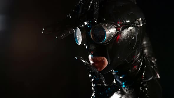 Closeup of a Head in a Black Latex Helmet Glasses and Drops of White Liquid alt