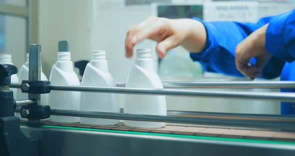 Closeup of a Woman's Hands That Places White Empty Bottles for Liquid Soap on a Conveyor Belt at a alt