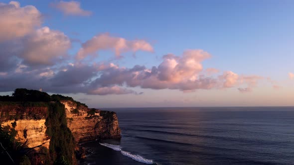 4K Time lapse of sunset at Uluwatu temple, Bali Indonesia. Clouds run on sky above sea waves. Cliff