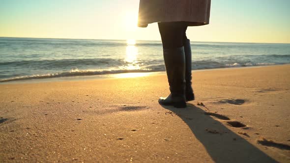 Woman Figure Shown From the Waist Down Walking Along the Beach Shore Wearing Long Boots