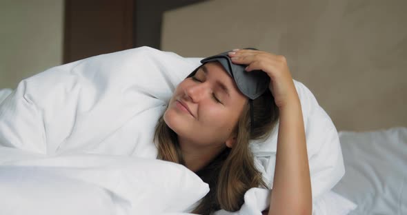 Woman Takes Off Mask From Head Lying Under Soft Duvet on Bed