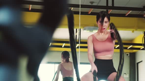 Asian young sport woman exercising workout by doing battle rope in gym stadium or fitness club. alt