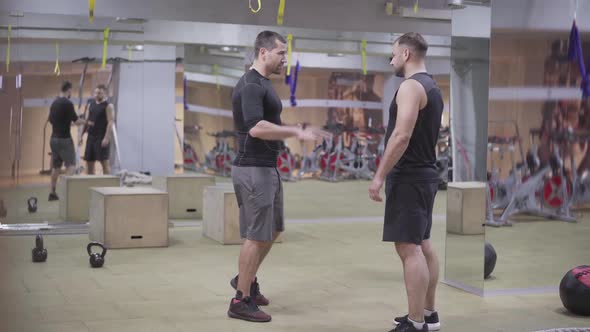 Wide Shot of Two Body-builders Talking in Gym. Strong Caucasian Sportsmen Standing in Sports Club alt