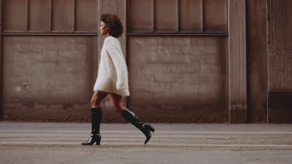 Smiling Young Woman With Windswept Afro Hair Walking Along Street alt
