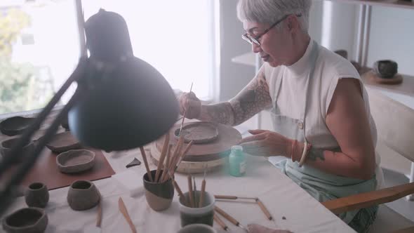 Asian elderly woman enjoying pottery work at home. alt