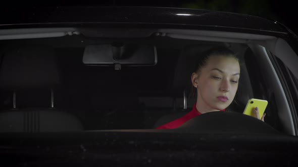 A Woman Drives a Car and Uses a Smartphone.