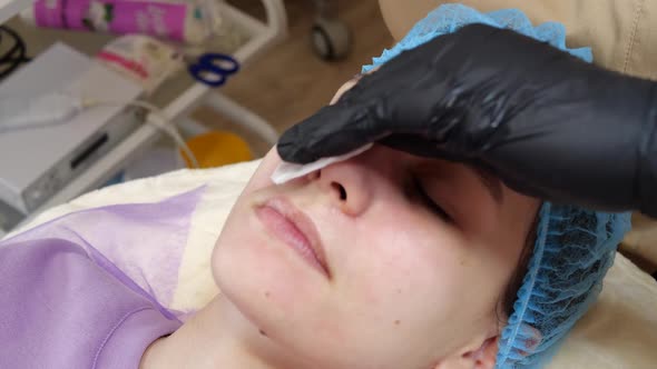 Closeup Cosmetician in Medical Gloves Applies Evenly Cosmetic Cream or Sunscreen to Female Face alt