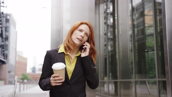 Businesswoman in city using smart phone with takeaway coffee